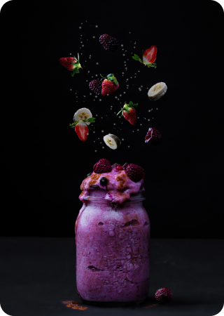 Milkshake roxo dentro de um pote de vidro com morangos, amoras e bananas voando